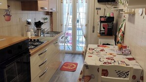 Una cocina con armarios de madera, una estufa a gas, un fregadero y un comedor con una mesa cubierta con un mantel de Hello Kitty.