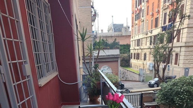 Un balcón con una mesa, sillas, una planta en maceta y un florero con flores.