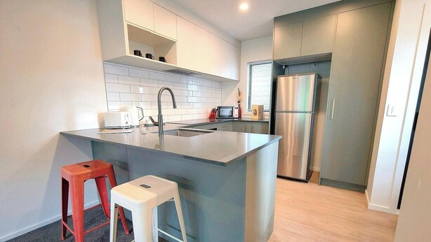 A modern kitchen with a central island, stainless steel appliances, and a red stool. - Relaxing Modern Stay in Upper Hutt Central (Upper Hutt)
