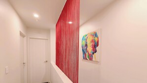 A hallway with a red vertical element, a white door, and a colorful elephant painting on the wall. - Relaxing Modern Stay in Upper Hutt Central (Upper Hutt)