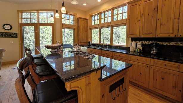 A kitchen with wooden cabinets, a large island with seating, and large windows. - Last Lift Lodge |  River Views, Grill, & Garage (Keystone)