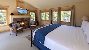 A bedroom with a large bed, a fireplace, two chairs, and a television. - Last Lift Lodge |  River Views, Grill, & Garage (Keystone)