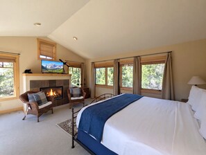 Ein Schlafzimmer mit einem großen Bett, einem Kamin, zwei Sesseln und einem Fernseher.