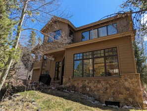A two-story house with a stone foundation, large windows, and a covered outdoor area. - Riverside 5BR Home: Scenic Serenity & Trail Bliss (Keystone)