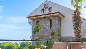 A dining area with a table set for two, a stone facade building in the background, and a view of greenery.