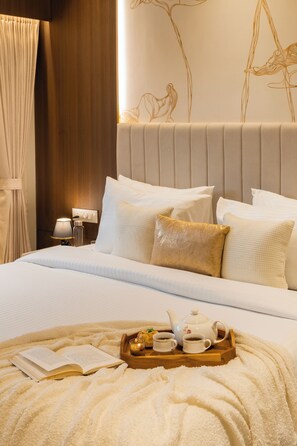 A neatly made bed with pillows, a bedside table with a lamp, and a tray with a teapot, cups, and a book.