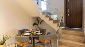 A dining area with a table set for four, a staircase, and a wooden door. - ELIVAAS Shourya Villa 3-BHK Villa (Udaipur)