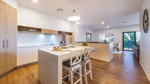 Una cuina moderna amb una illa central, armaris de fusta i zona de menjador amb cadires blanques.