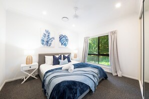 Ein Schlafzimmer mit einem Bett, Nachttischen, einem Fenster mit Vorhängen und Wandbildern.