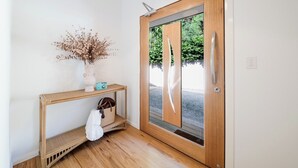 Una porta de fusta amb un panell de vidre, una paret blanca, una petita taula de consol amb un vas i una làmpada, i una tovallola blanca penjada a la taula de consol.