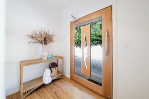 Eine Holztür mit Glasfenster, eine weiße Wand, ein kleiner Konsolentisch mit Vase und Lampe, und ein weißes Handtuch, das am Konsolentisch hängt.