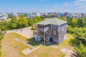 A multi-story building with a balcony, a fire pit in the yard, and a view of other houses in the background. - Brand New Oceanside Salvo Home, Dog Friendly with Hot Tub (Salvo)