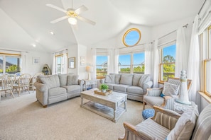 A spacious living room with a ceiling fan, a round mirror, and a view of the outside. - Brand New Oceanside Salvo Home, Dog Friendly with Hot Tub (Salvo)