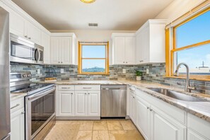 A modern kitchen with white cabinets, stainless steel appliances, a dishwasher, and a large window with a view. - Brand New Oceanside Salvo Home, Dog Friendly with Hot Tub (Salvo)