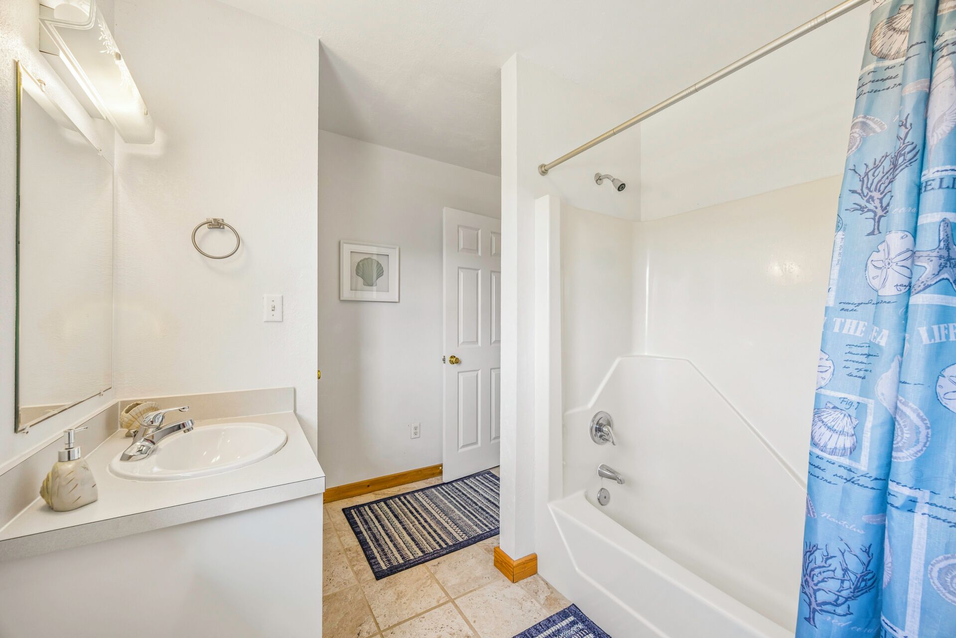 A bathroom with a sink, mirror, shower, and a door leading to another room.