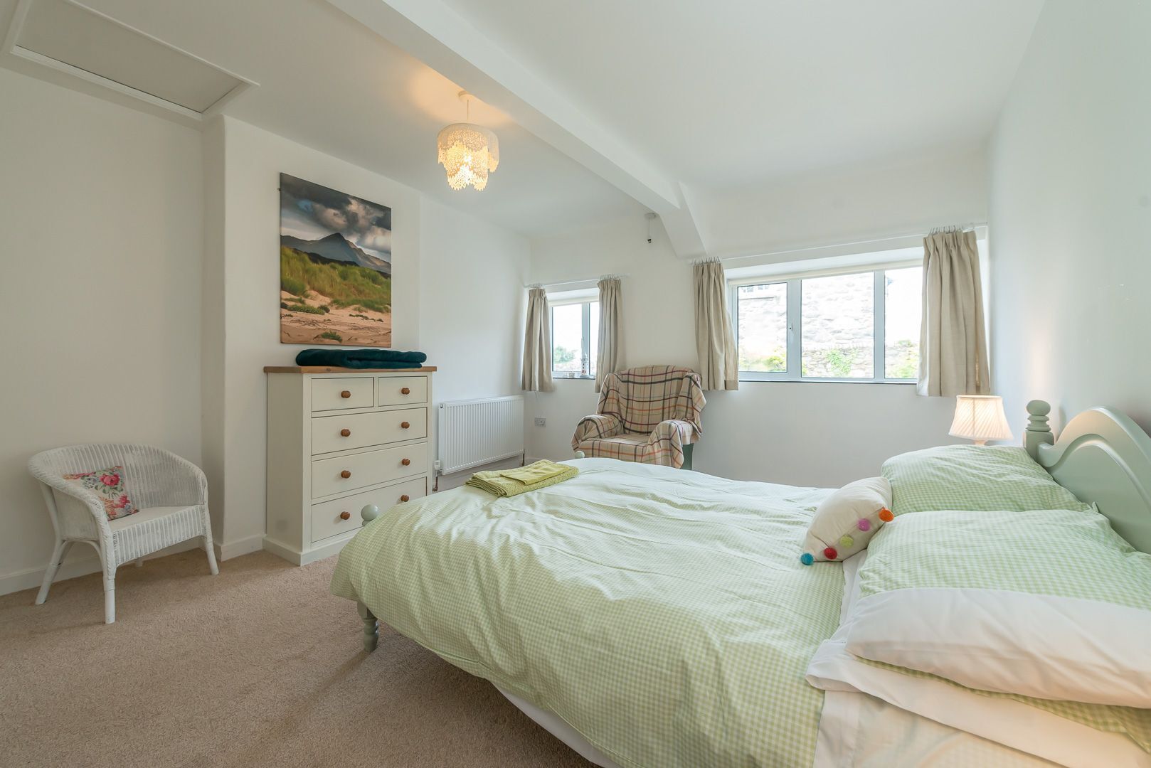 Een slaapkamer met een bed, een stoel, een dressoir, een schilderij en een raam.