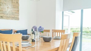 A dining table with chairs, a vase with flowers, and bottles of wine. - Spacious Four Bedroom Holiday Accommodation On Anglesey | Bryndeusant (Holyhead, Ynys Môn)