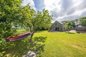 A grassy area with a hammock, a stone building, and a wooden structure. - Large Barn Conversion on a Working Farm on the Llŷn Peninsula | Rhiwal (Pwllheli)