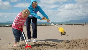 Two people on a sandy beach with a clear sky and distant mountains. - Modern Four Bedroom Property with Sea Views | Tan-Y-Foel (Dyffryn Ardudwy)