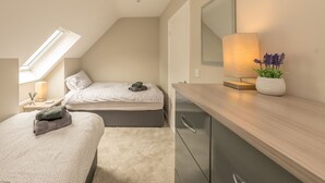A bedroom with a skylight, a bed with pillows, a bedside table with a lamp, a dresser, and a potted plant. - Modern Four Bedroom Property with Sea Views | Tan-Y-Foel (Dyffryn Ardudwy)
