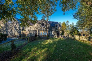 A stone house with a large front yard, a wooden fence, and a bench. - Three Bedroom Cottage With Views To The Sea | Stabal-Bryn-Hir (Criccieth)