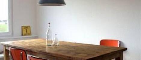 A dining area with a wooden table, two red chairs, a hanging light fixture, and a window with a view.