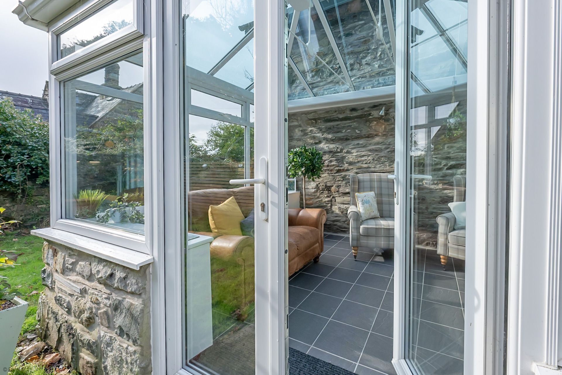 A conservatory with stone walls, a tiled floor, and seating areas with cushions.