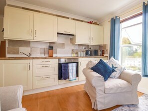 A modern kitchen with white cabinets, a built-in oven, and a window with blue curtains. - Berkeley View (Looe)