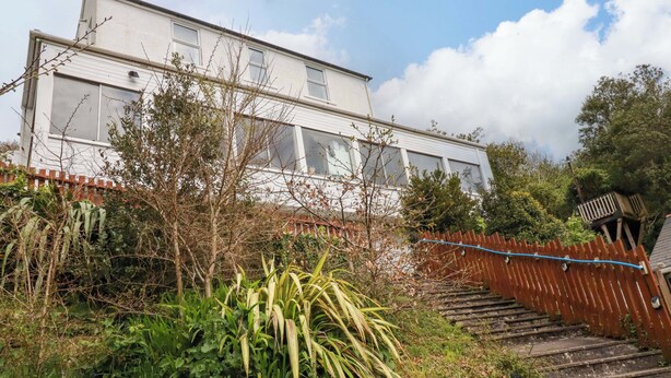 A two-story building with a white exterior, a wooden fence, and a staircase leading up to the entrance. - Berkeley View (Looe)