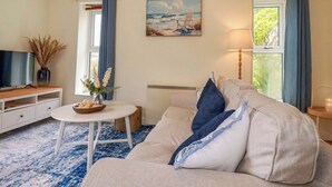 A living room with a sofa, a TV, a table with a vase, and a painting on the wall. - Berkeley View (Looe)
