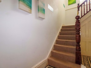 Una escalera alfombrada con barandilla de madera, paredes blancas y un letrero de salida verde.