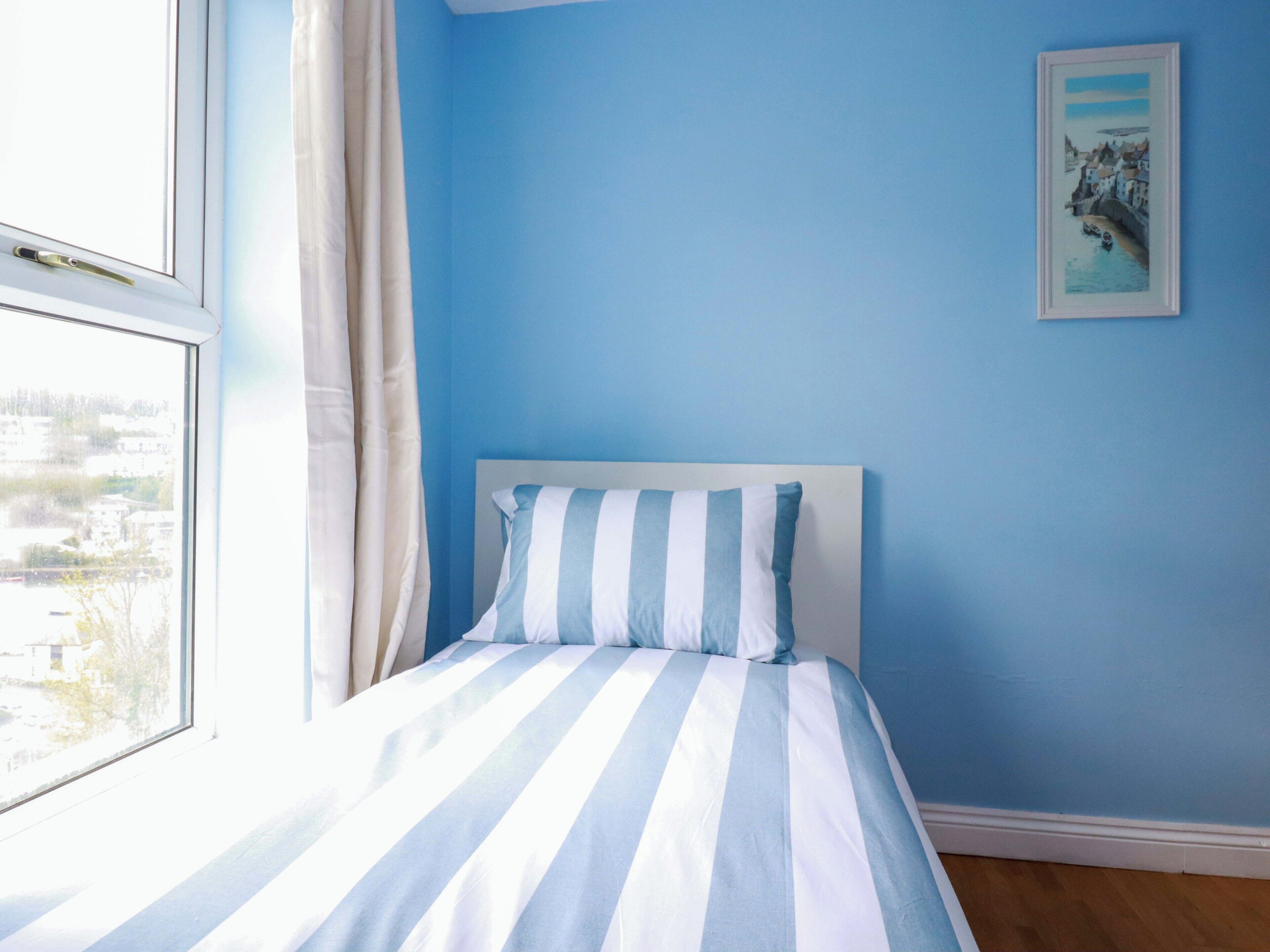 A bedroom with a bed, a window, and a painting on the wall.