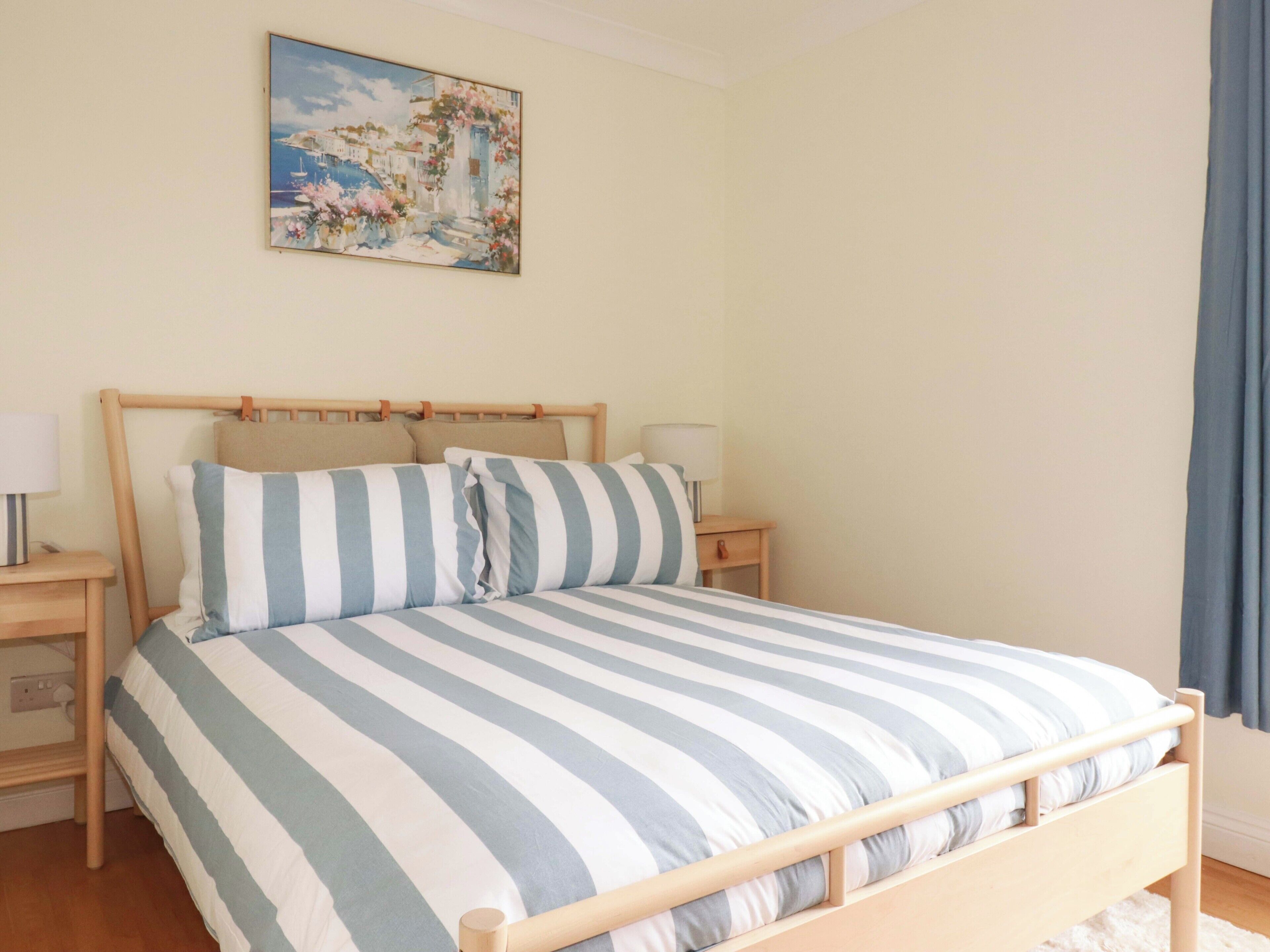 A bed with striped bedding, wooden headboard, bedside tables with lamps, and a painting on the wall.