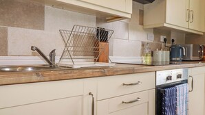 A kitchen with a sink, a dish rack, a kettle, and a coffee maker. - Berkeley View (Looe)