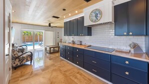A modern kitchen with dark blue cabinets, a wooden countertop, and a large clock. - Aloha House: Beautiful North End pool home (Anna Maria)