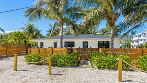 A house with a gravel driveway, a wooden fence, and palm trees. - Aloha House: Beautiful North End pool home (Anna Maria)