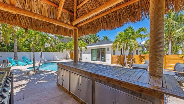 A covered outdoor area with a pool, wooden deck, and metal cabinets. - Aloha House: Beautiful North End pool home (Anna Maria)