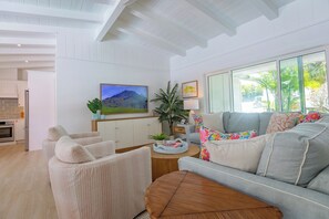 Ein modernes Wohnzimmer mit grauem Sofa, beigen Sesseln, einem Holztisch und einem großen Fenster mit Blick auf Grünflächen.