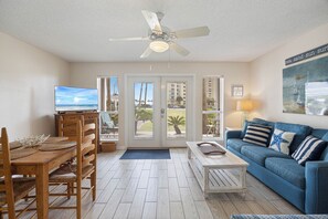 Ein Wohnzimmer mit Deckenventilator, Fernseher, blauem Sofa, Esstisch aus Holz und Stühlen.