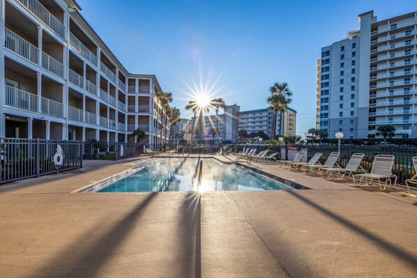 A pool area with sunlit water, lounge chairs, and multi-story buildings with balconies. - Sea Sparrow Nest by PKRM (Pensacola)