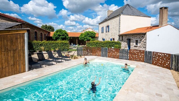 Ein Schwimmbecken mit klarem Wasser, umgeben von Steinbauten und einem Holzzaun.