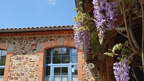 Ein Steinhaus mit einer blauen Tür, einem Fenster und einem hängenden violetten Blumenstrauß.