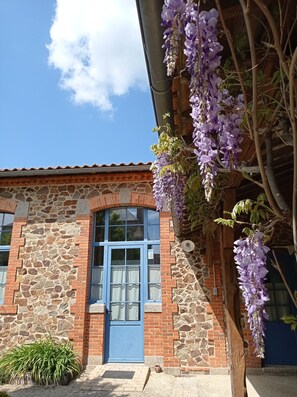 A stone building with a blue door, a window, and a hanging purple flower. - 40 minutes from Le PUY DU FOU Gîte with swimming pool and private garden (Montaigu-Vendée)