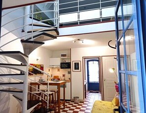 A compact apartment with a spiral staircase, a kitchen, a dining area, and a checkered floor. - 40 minutes from Le PUY DU FOU Gîte with swimming pool and private garden (Montaigu-Vendée)