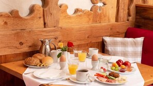 A breakfast setup with bread, eggs, fruit, and beverages on a wooden table with a decorative headboard.