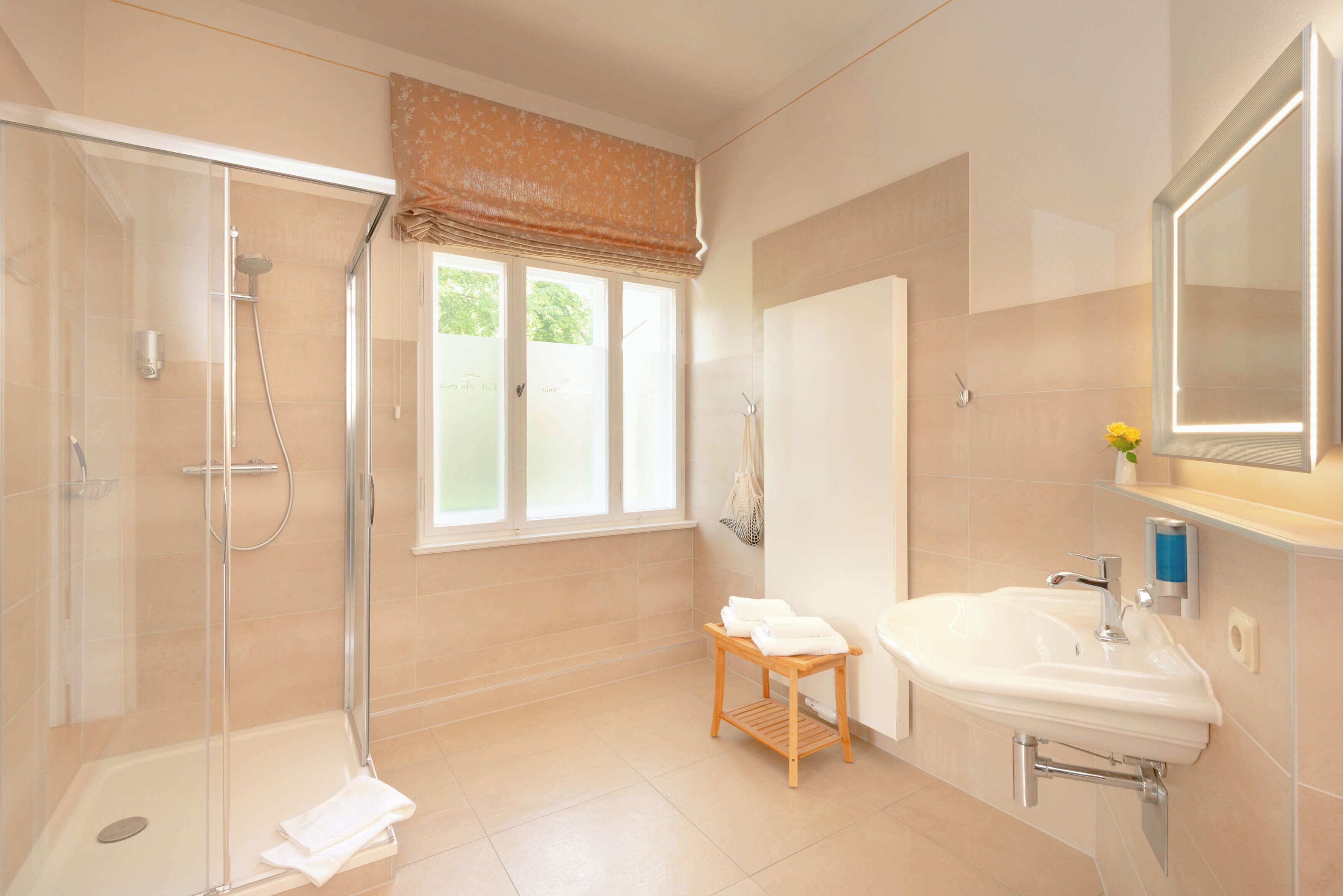 A modern bathroom with a glass-enclosed shower, a sink with a mirror, and a window with a view.