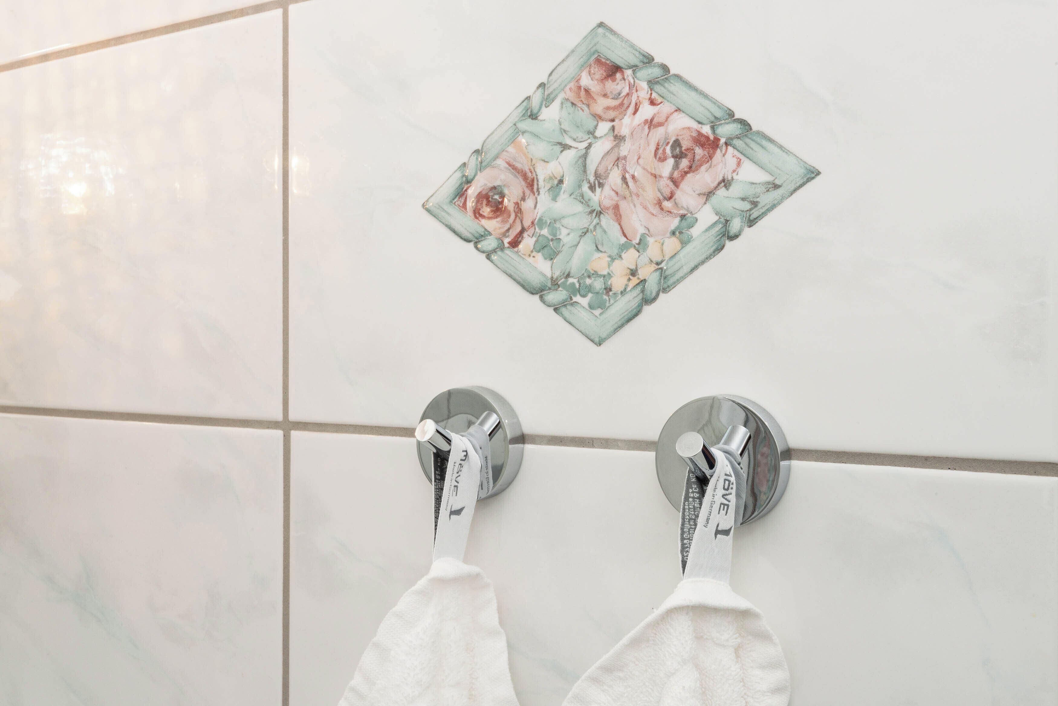 A bathroom with a floral tile design, two towel racks with white towels, and a tiled floor.