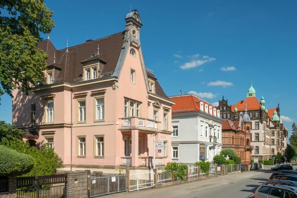 A historic building with a prominent clock tower, a balcony, and a sign indicating it is a hotel.