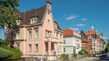 A historic building with a prominent clock tower, a balcony, and a sign indicating it is a hotel.