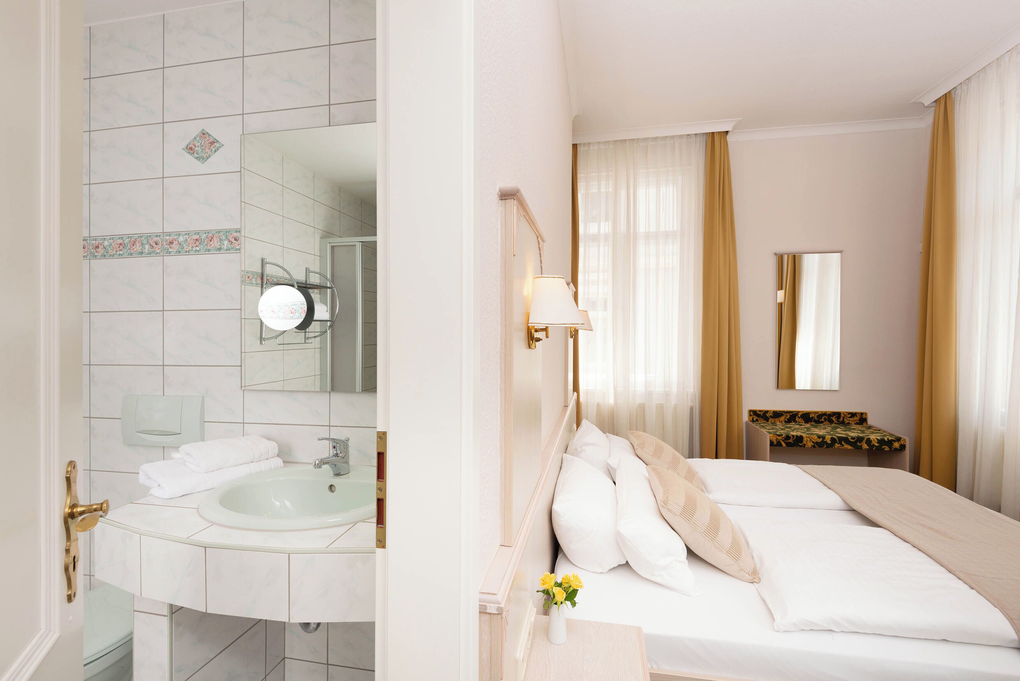 A hotel room with a bathroom, a bed, a bedside table, and a mirror.